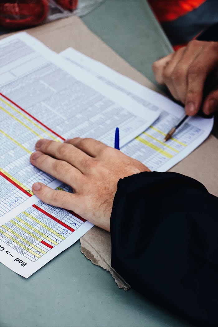 Hands with pen analyzing spreadsheets at a desk, focusing on data and statistics.